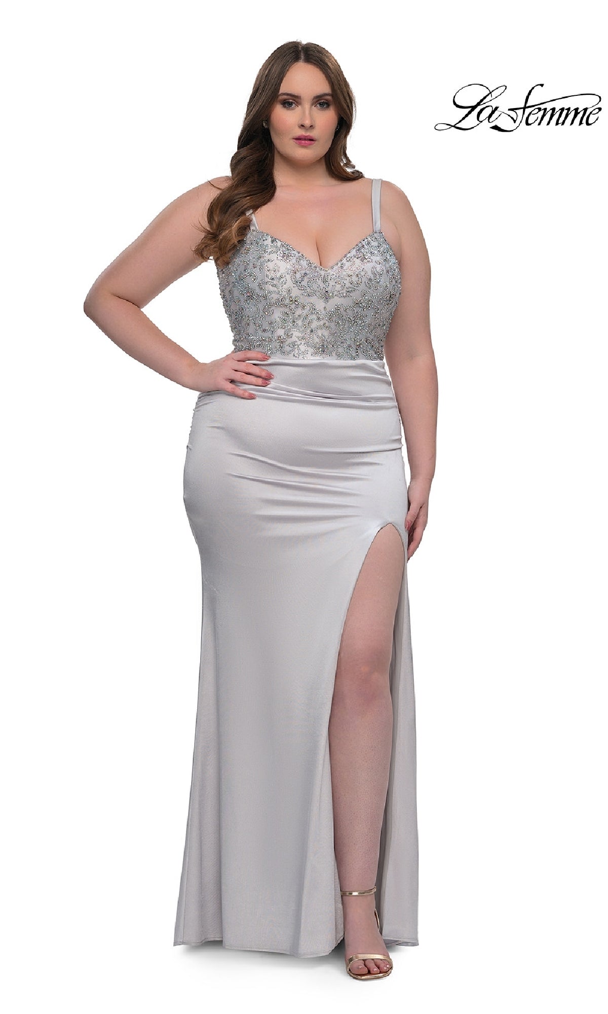 A woman poses against a white background in the La Femme 32430 plus-size long satin prom dress with a rhinestone beaded bodice, thick straps, and high slit, paired with open-toe heels. The